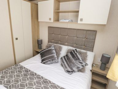 A bedroom with a bed with pillows and a blanket a headboard nightstands with lamps and cabinets at 116 Woodpecker Lodge in Gilfachrheda near Llanarth
