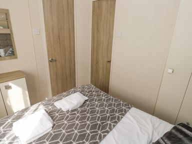 A bedroom with a bed covered with a patterned blanket and folded towels on top in 116 Woodpecker Lodge Gilfachrheda near Llanarth