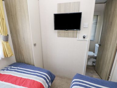 A bedroom with two beds a wall-mounted TV and a partially open door leading to a bathroom at 116 Woodpecker Lodge in Gilfachrheda near Llanarth