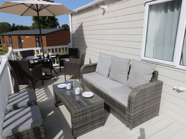 An outdoor patio with a wicker sofa, coffee table, dining table with chairs, and an umbrella at 116 Woodpecker Lodge in Gilfachrheda near Llanarth