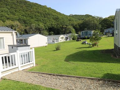 Green grassy area with several white lodges and trees near a wooded hill at 116 Woodpecker Lodge Gilfachrheda near Llanarth