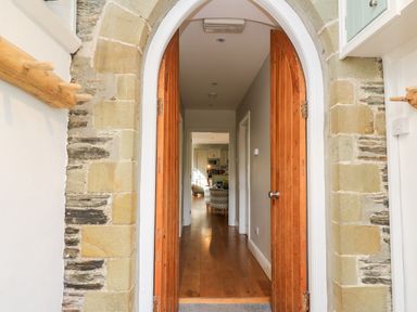 A stone arched doorway with wooden double doors opening to a hallway with hardwood flooring leading to a living area at Upper Vestry in Llangrannog