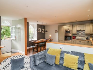 An open plan living room with sofa and armchair next to a dining table and kitchen at Upper Vestry in Llangrannog