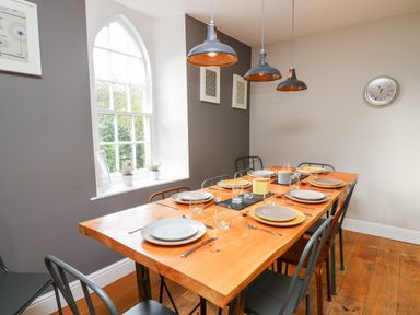A dining room with a wooden table set with plates glasses and cutlery metal chairs and a window at Upper Vestry in Llangrannog
