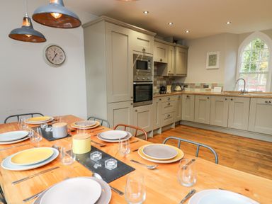 A kitchen with a wooden dining table set with plates and glasses and grey cabinets at Upper Vestry in Llangrannog
