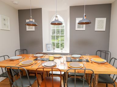 A dining room with a wooden table set for eight with plates glasses and cutlery at Upper Vestry in Llangrannog