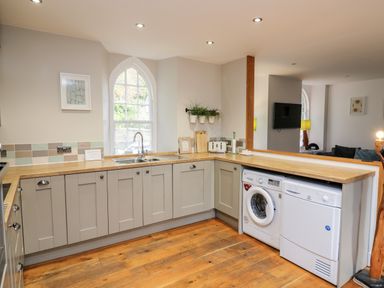 A kitchen with gray cabinets wooden countertops a washing machine dryer a window and plants at Upper Vestry in Llangrannog