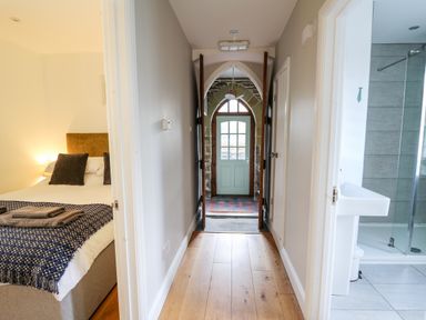 A hallway with a wooden floor leading to a door with glass panels with a bedroom on the left and a bathroom on the right at Upper Vestry in Llangrannog