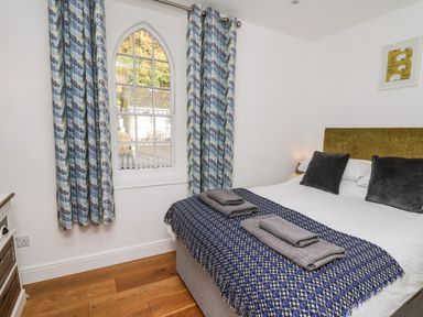 A bedroom with a double bed a blue patterned blanket folded towels on the bed and a window with patterned curtains at Upper Vestry in Llangrannog