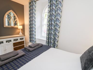 A bedroom with a bed folded towels curtains a cabinet a lamp and a wall mirror at Upper Vestry in Llangrannog