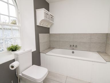 A bathroom with a toilet a bathtub and a window with lace curtains at Upper Vestry in Llangrannog