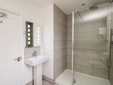 A bathroom with a white sink and mirror next to a glass shower enclosure at Upper Vestry in Llangrannog
