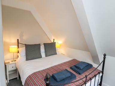 A bedroom with a double bed with two gray pillows bedside tables with lamps and folded towels on the bed at Upper Vestry in Llangrannog