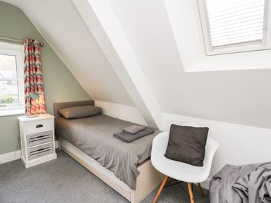 A bedroom with a single bed gray bedding a white nightstand with a lamp a white chair with a dark cushion and a skylight at Upper Vestry in Llangrannog