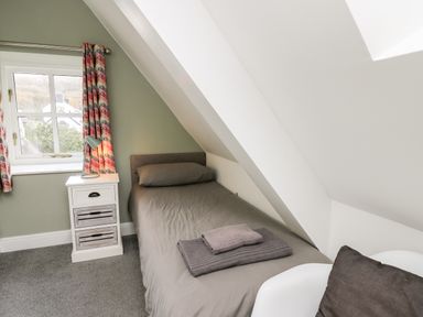 A small bedroom with a single bed nightstand with lamp and window with colorful curtains at Upper Vestry in Llangrannog