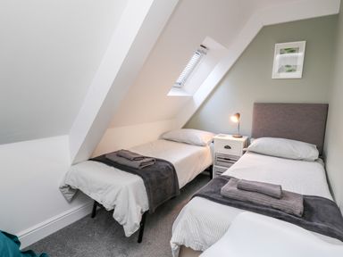 A bedroom with two single beds side by side with a nightstand and lamp between at Upper Vestry in Llangrannog