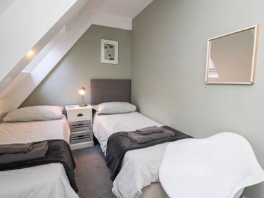 A bedroom with two single beds a white chair a nightstand with a lamp and a framed picture on the wall at Upper Vestry in Llangrannog