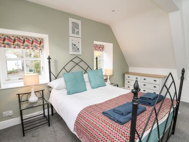 A bedroom with a bed with blue pillows and folded towels on a blanket a dresser and lamps on tables at Upper Vestry in Llangrannog