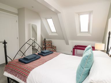 A bedroom with a bed with blue pillows a patterned armchair a full length mirror and two windows at Upper Vestry in Llangrannog