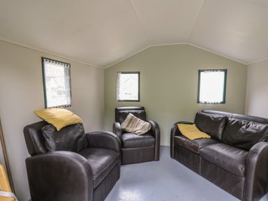 A small room with three black leather chairs and cushions under three small windows at Upper Vestry in Llangrannog