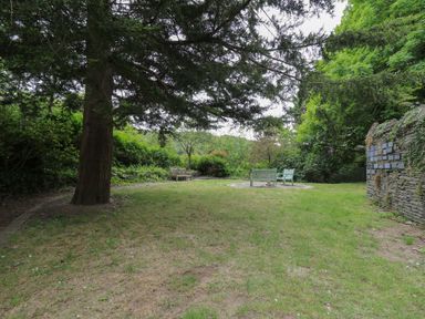 A grassy garden area with benches under trees and a stone wall with plaques at Upper Vestry in Llangrannog