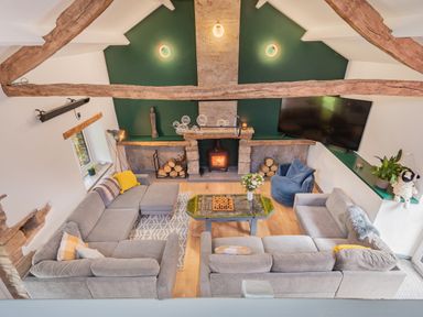 A living room with grey sofas a wood burning stove and a TV mounted on the wall at The Waterfall Retreat in Orton