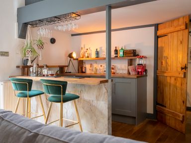 A home bar area with two green bar stools and bottles on shelves at The Waterfall Retreat in Orton
