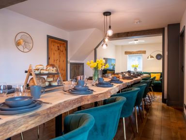 A dining room with a long wooden table set with blue plates and cups and teal chairs at The Waterfall Retreat in Orton