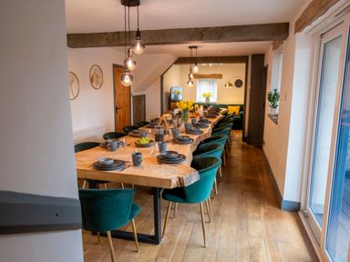 A dining room with a long wooden table set with dishes and green chairs at The Waterfall Retreat in Orton