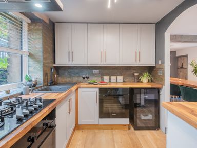 A kitchen with white cabinets wooden countertops a gas stove oven sink and wine cooler at The Waterfall Retreat in Orton