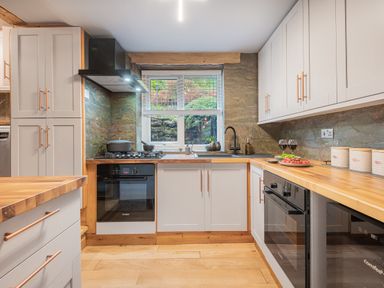 A kitchen with wooden countertops white cabinets gas stove oven and a sink below a window at The Waterfall Retreat in Orton