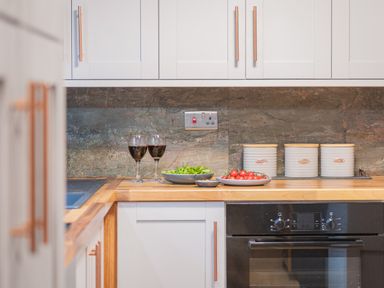 A kitchen countertop with two glasses of red wine plates with salad and tomatoes and three white canisters above a built in oven at The Waterfall Retreat in Orton