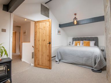 A bedroom with a bed with gray bedspread and orange pillows and a wooden door open at The Waterfall Retreat in Orton