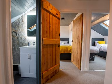 A hallway view showing a bathroom with a sink and mirror and two bedrooms with beds and wooden doors at The Waterfall Retreat in Orton