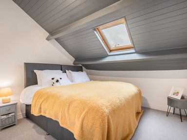 A bedroom with a bed covered by a yellow blanket a nightstand with a lamp and a small stool with a framed picture at The Waterfall Retreat in Orton