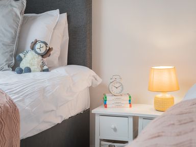 A bedroom with a bed a stuffed toy on pillows a bedside table with books a clock and a lamp at The Waterfall Retreat in Orton