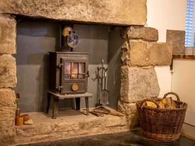 A stone fireplace with a wood-burning stove a basket of firewood and fireplace tools at The Waterfall Retreat in Orton