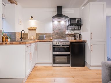 A kitchen with white cabinets wooden countertops and appliances at The Waterfall Retreat in Orton