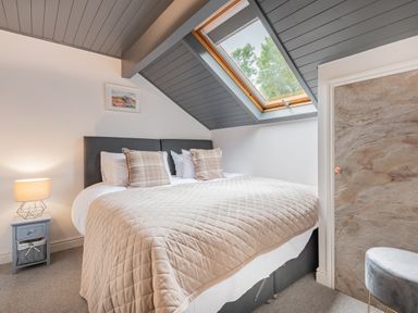 A bedroom with a large bed pillows and a quilt a nightstand with a lamp a skylight window and a small stool at The Waterfall Retreat in Orton