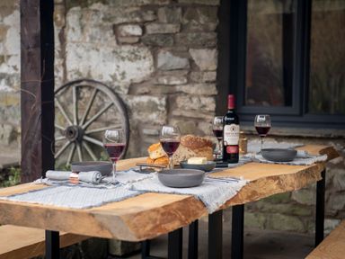 An outdoor wooden table set with four wine glasses with red wine gray bowls bread and a bottle of wine at The Waterfall Retreat in Orton
