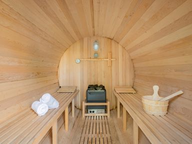 An indoor wooden sauna with two benches a heater with stones white rolled towels and a wooden bucket with a ladle at The Waterfall Retreat in Orton