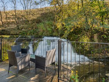 An outdoor seating area with four chairs and a table next to a waterfall and river at The Waterfall Retreat in Orton