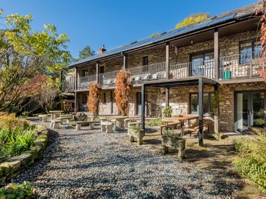 An outdoor garden area with stone benches tables and a wooden pergola in front of a stone building with a balcony at The Waterfall Retreat in Orton