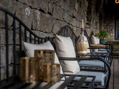 A stone patio with black metal chairs and cushions with decorative items on tables at The Waterfall Retreat in Orton