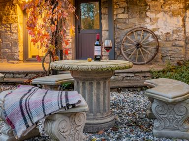 An outdoor stone table and benches with a bottle of wine and glass in front of a stone building at The Waterfall Retreat in Orton