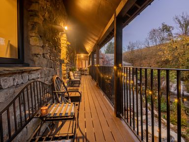 A covered wooden balcony with benches and string lights overlooking a garden at The Waterfall Retreat in Orton
