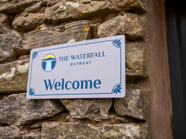 A welcome sign mounted on a stone wall at The Waterfall Retreat in Orton
