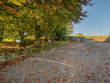 A gravel parking area with marked spaces next to trees and a wooden gate at The Waterfall Retreat in Orton