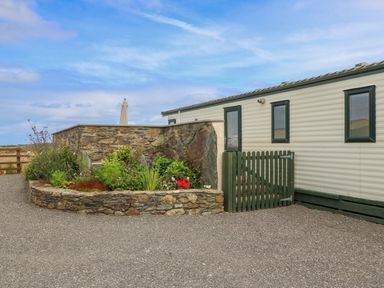 An exterior view of a mobile home with green windows and a small garden with plants and flowers at Cae Gog Near Cemaes Bay