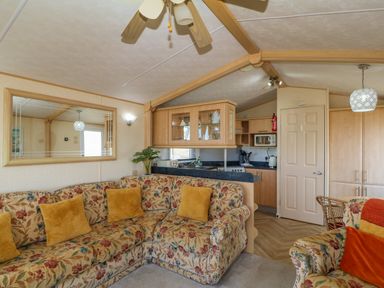 A living room with floral sofas and yellow cushions next to a kitchen at Cae Gog Near Cemaes Bay